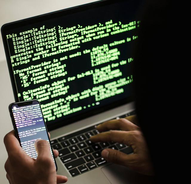 Gambar oleh https://www.pexels.com/photo/unrecognizable-hacker-with-smartphone-typing-on-laptop-at-desk-5935791/