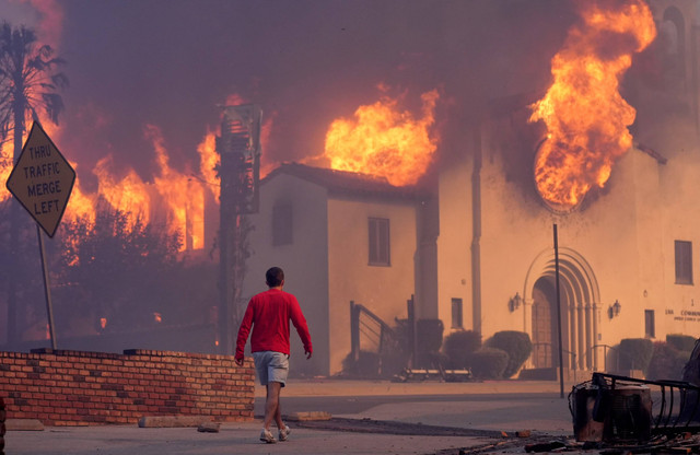 Seorang pria berjalan di depan Gereja Komunitas Altadena yang terbakar di kawasan pusat kota Altadena, Pasadena, California, pada 8 Januari 2025. Foto: Chris Pizzello/AP Photo