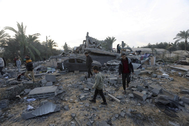 Tiga warga melintas dengan latar belakang bangunan yang hancur akibat serangan Israel di Jalur Gaza Tengah, Rabu (15/1/2025). Foto: Ramadan Abed/REUTERS