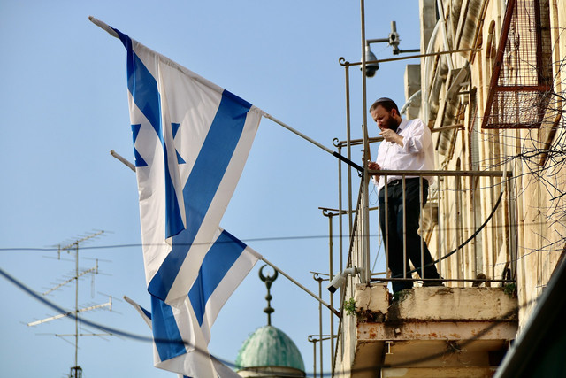 Gambar seorang pria memegang bendera Israel. Sumber dari Jorge Fernández Salas melalui Unsplash.