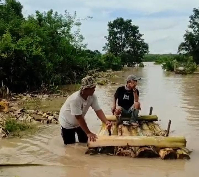 Warga menyeberangi jalan yang tergenang air menggunakan perahu. | Foto: Istimewa