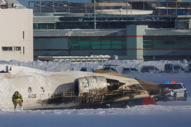 Petugas tanggap darurat berada di dekat pesawat Delta Airlines terguling saat mendarat di Bandara Toronto Pearson, Toronto, Ontario, Kanada, Senin (17/2/2025). Foto: Arlyn McAdorey/REUTERS