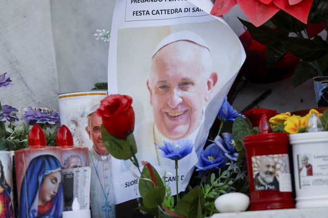 Foto Paus Fransiskus diletakkan di samping lilin dan bunga di dasar patung mendiang Paus Yohanes Paulus II di luar Rumah Sakit Gemelli tempat Paus Fransiskus dirawat, di Roma, Italia, Minggu (23/2/2025). Foto: Ciro De Luca/REUTERS