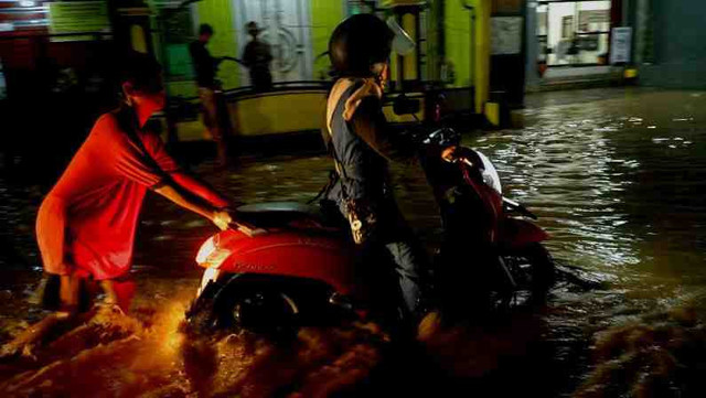 Warga membantu mendorong sepeda motor yang mogok saat melintasi jalan raya terendam banjir di simpang empat Cuwiri, Tulungagung, Jawa Timur, Rabu (26/2/2025).  Foto: ANTARA FOTO/Destyan Sujarwoko