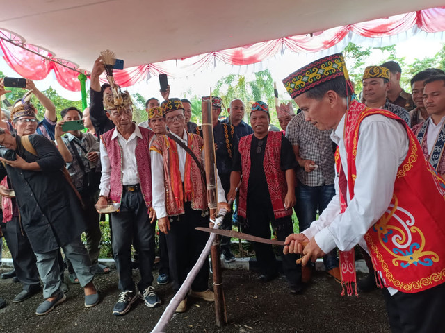 Bupati Sintang, Gregorius Herkulanus Bala memotong hompong yang merupakan bagian dari ritual adat Dayak sebelum memasuki rumah dinas. Foto: Diskominfo Sintang