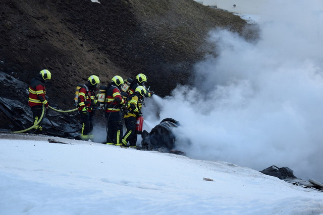 Petugas pemadam kebakaran bekerja di lokasi jatuhnya pesawat kecil di La Punt Chamues-ch, Swiss, Selasa (18/3/2025). Foto: Polisi Graubuenden/HO/REUTERS