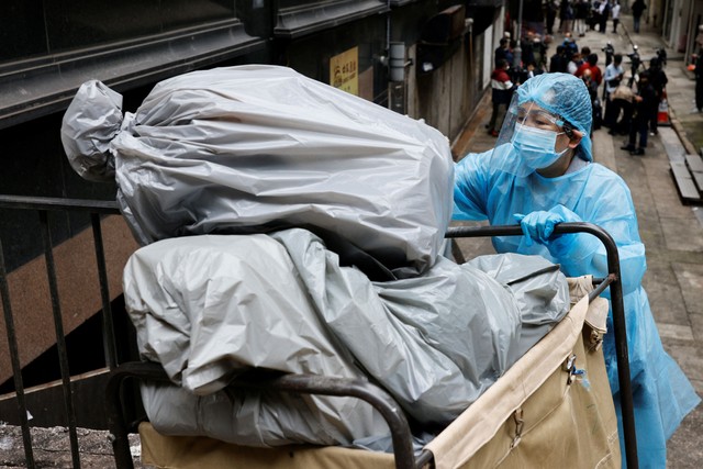 Seorang petugas kebersihan menggunakan alat pelindung diri (APD) membuang sampah di luar hotel karantina selama pandemi penyakit virus corona (COVID-19) di Hong Kong, China, Sabtu (2/4/2022). Foto: Tyrone Siu/REUTERS