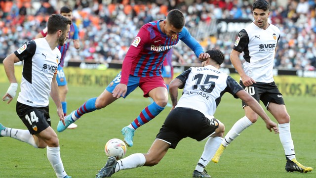 Pemain Barcelona Ferran Torres duel dengan pemain Valencia Jose Gaya Pena dan Omar Alderete saat pertandingan liga Spanyol di stadion Mestalla di Valencia Minggu (20/2/2022). Foto: Jose Jordan/AFP