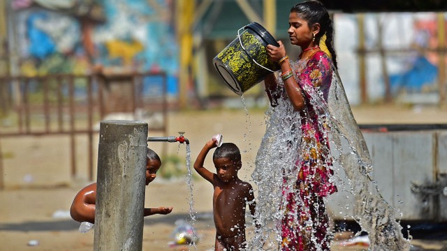 Seorang wanita dan dua orang anak menyiramkan air ke badan mereka akibat cuaca panas ekstrem yang melanda India. Foto: SANJAY KANOJIA / AFP