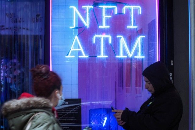 Orang-orang melewati "NFT ATM," sebuah etalase kecil yang menampung mesin penjual otomatis non-fungible token (NFT) pertama Neon di distrik keuangan Lower Manhattan, New York City,  AS, Selasa (1/3/2022).
 Foto: Brendan McDermid/Reuters