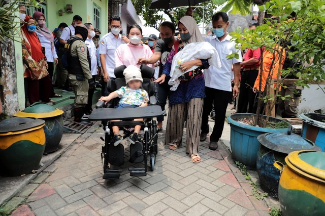 Sharga Raditya Nugraha saat mencoba stroller bantuan dari Pemkot Surabaya. Sedangkan sang adik, Tanaka, dalam gendongan sang ibu. Foto-foto: Diskominfo Surabaya