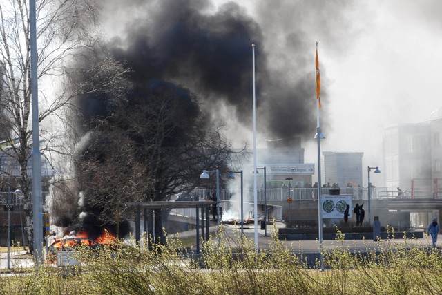 Asap mengepul dari mobil yang terbakar selama kerusuhan unjuk rasa menentang pembakaran Al-Quran oleh politisi anti-Muslim Denmark Rasmus Paludan di Navestad, Norrkoping, Swedia. Foto: Ulf Wigh/Wighsnews/via REUTERS