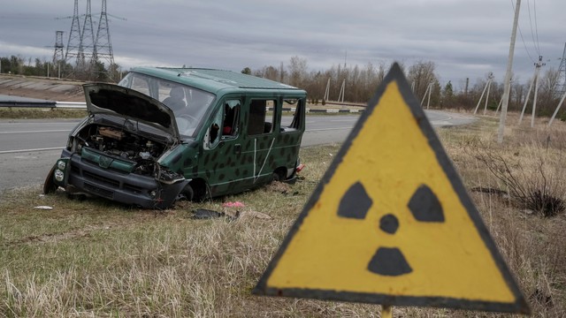 Sebuah mobil hancur di dekat struktur New Safe Confinement (NSC) di atas sarkofagus tua yang menutupi reaktor keempat yang rusak di Pembangkit Listrik Tenaga Nuklir Chernobyl, di Chernobyl, Ukraina, Sabtu (16/4/2022). Foto: Gleb Garanich/REUTERS