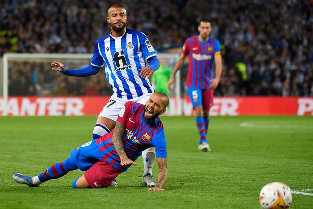 Pemain Barcelona Dani Alves terjatuh di sebelah pemain Real Sociedad Rafinha di Reale Arena, San Sebastian, Spanyol, Kamis (21/4/2022). Foto: Ander Gillenea/AFP