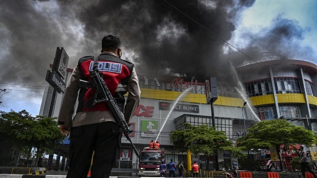 Seorang petugas polisi menyaksikan pemadam kebakaran berusaha memadamkan api di pusat perberlanjaan Suzuya Mall, di Banda Aceh, Aceh pada Senin (4/4/2022). Foto: Chaideer Mahyuddin/AFP