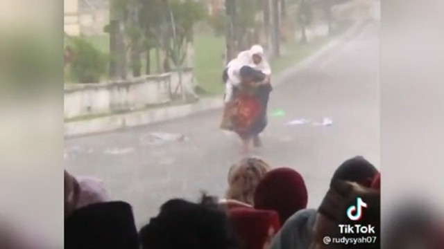 Aksi seorang pria gendong seorang ibu yang terjebak di bawah hujan badai yang terjadi di halaman Kantor Gubernur Sumatera Barat, Senin 2 Mei 2022. Foto: @rudysaitama