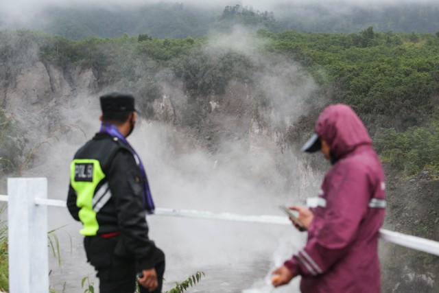 Seorang petugas polisi dan seorang warga berdiri di dekat pagar saat lahar panas mengalir di Kali Gendol, Cangkringan, Yogyakarta (10/3). Foto: Dwi Oblo/Reuters