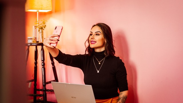 Foto orang selfie dengan hp di depan laptop. Foto: Unsplash/Mateus Campos Felipe.