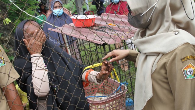 Seorang ibu menangis di balik pagar besi akibat tidak mendapatkan kartu antrean minyak goreng di Kendari, Sulawesi Tenggara, Selasa (15/3/2022). Foto: Jojon/Antara Foto
