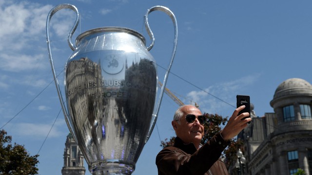 Seorang pria mengambil foto selfie di depan replika trofi Liga Champions UEFA di jalan Aliados di Porto. Foto: Miguel Riopa/AFP