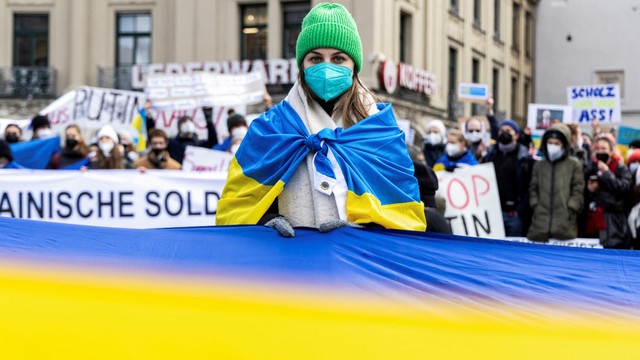 Seorang demonstran memegang bendera besar dengan warna nasional Ukraina saat protes invasi Rusia ke Ukraina, di depan gerbang Brandenburg di Berlin, Jerman, Sabtu (26/2/2022). Foto: Christian Mang/REUTERS