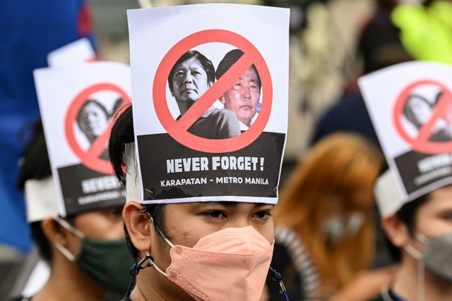 Para pengunjuk rasa menggunakan poster di kepala selama demonstrasi untuk memperingati 36 tahun gerakan Kekuatan Rakyat yang menggulingkan mendiang diktator Filipina Ferdinand Marcos di Manila, Jumat (25/2/2022). Foto: Ted ALJIBE / AFP
