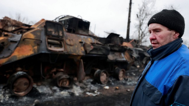 Seorang penduduk setempat berdiri di samping kendaraan militer yang hancur, di kota Bucha di wilayah Kiev, Ukraina Rabu (1/3/2022). Foto: Serhii Nuzhnenko/REUTERS