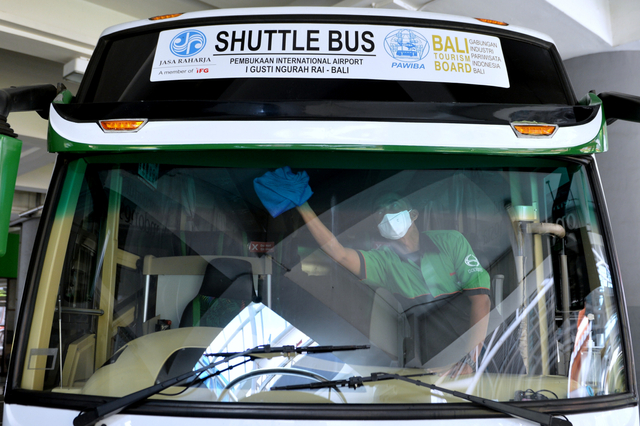 Petugas membersihkan kaca bus yang disiapkan untuk mengangkut penumpang internasional menuju hotel karantina di Bandara Internasional I Gusti Ngurah Rai, Badung, Bali, Kamis (14/10/2021). Foto: Fikri Yusuf/ANTARA FOTO