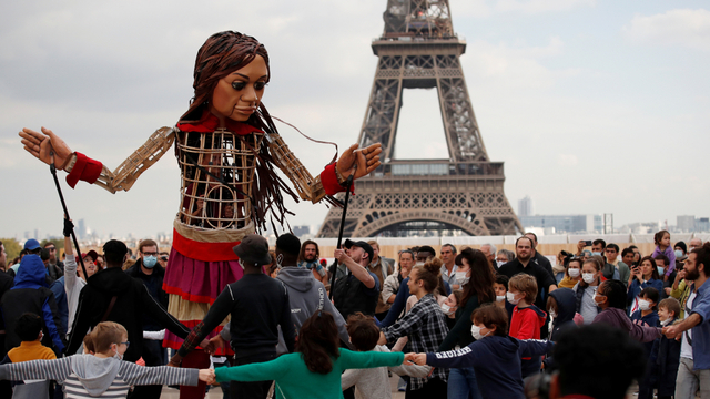 Orang-orang berkumpul di sekitar Little Amal, boneka setinggi 3,5 meter yang menggambarkan pengungsi Suriah di alun-alun Trocadero dekat Menara Eiffel di Paris, Prancis, Jumat (15/10). Foto: Gonzalo Fuentes/REUTERS