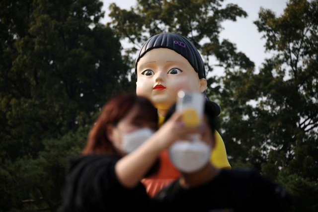 Warga swafoto dengan boneka raksasa dalam serial Squid Game yang dipamerkan di sebuah taman di Seoul, Korea Selatan. Foto: Kim Hong- Jihee/REUTERS