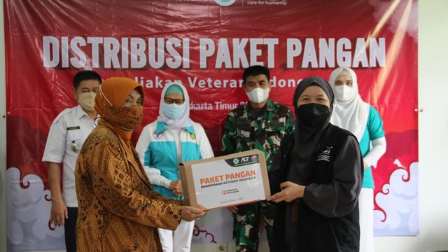 Kepala Cabang ACT Jakarta Timur (kanan) memberikan bantuan paket pangan kepada salah satu perwakilan janda veteran di Gedung Koramil 03 Pasar Rebo, Jakarta Timur 