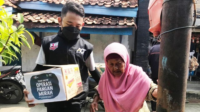 Relawan MRI-ACT sedang membantu seorang lansia membawa makanan ke rumahnya.