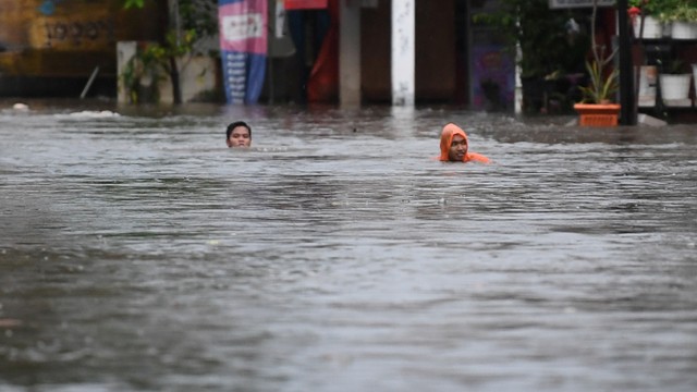 Warga melintasi banjir di Pela Mampang, Jakarta, Minggu (7/11/2021). Foto: Akbar Nugroho Gumay/Antara Foto