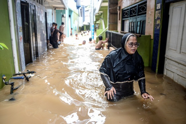 Warga melintasi banjir yang merendam kawasan Kebon Pala, Kampung Melayu, Jatinegara, Jakarta Timur, Senin (8/11/2021). Foto: M Risyal Hidayat/Antara Foto