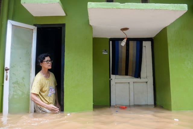 Seorang warga berdiri di jendela rumahnya ketika banjir merendam di kawasan Kebon Pala, Kampung Melayu, Jatinegara, Jakarta Timur, Senin (8/11/2021). Foto: M Risyal Hidayat/Antara Foto