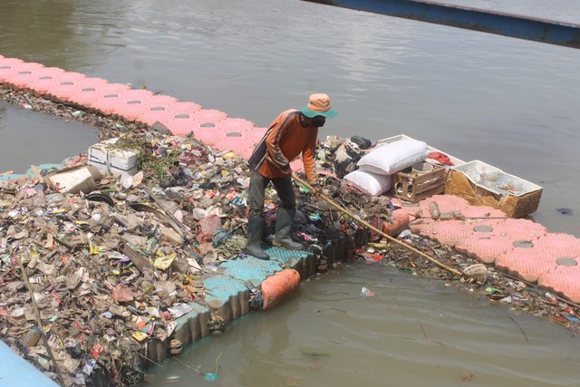 Foto petugas kebersihan sedang menggiring sampah di sungai. Photo by Lynea Grandisa