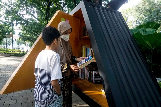 Seorang anak bersama orang tuadnya membaca buku di perpustakaan mini Taman Suropat, Jakarta, Minggu (21/11).  Foto: Iqbal Firdaus/kumparan