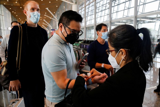 Seorang staf bandara mengenakan gelang pada seorang pelancong setibanya di Bandara Internasional Kuala Lumpur (KLIA) di bawah program Jalur Perjalanan Vaksinasi Malaysia-Singapura (VTL). Foto: REUTERS/Lai Seng Sin