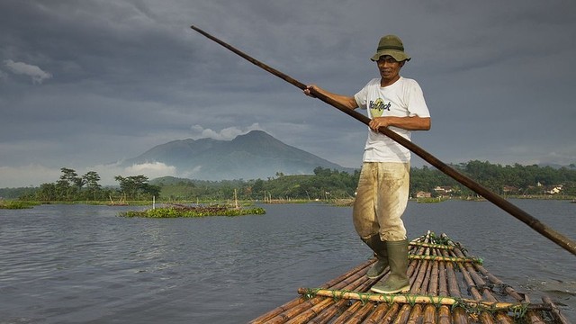 Seorang pria mengayuh rakit bambu di Situ Bagendit dengan latar belakang pemandangan Gunung Guntur.