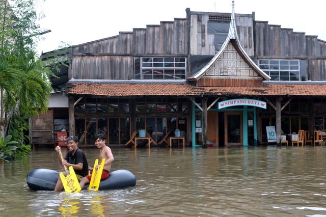 Warga menaiki kasur angin untuk menerobos banjir yang menggenangi kawasan Legian, Kuta, Badung, Bali, Senin (6/12/2021). Foto: Fikri Yusuf/Antara Foto