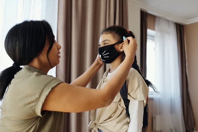 foto seorang ibu yang memakaikan masker kepada anaknya (Photo by August de Richelieu from Pexels.com)