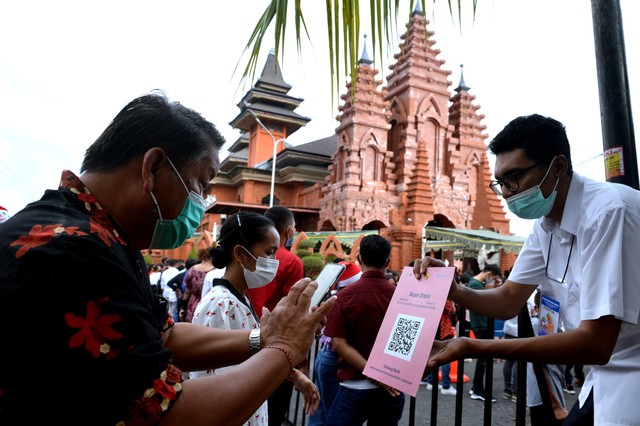 Umat Katolik memindai kode batang dengan aplikasi PeduliLindungi saat Misa Malam Natal di Gereja Katolik Roh Kudus Katedral Denpasar, Bali, Jumat (24/12/2021). Foto: Fikri Yusuf/Antara Foto