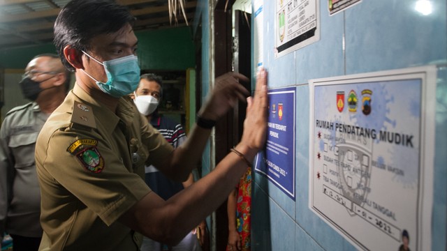 Lurah Jebres, Solo, Lanang Aji Laskito menempelkan stiker di rumah yang ditinggali pemudik Nataru, Senin (27/12/2021) malam. FOTO: Agung Santoso