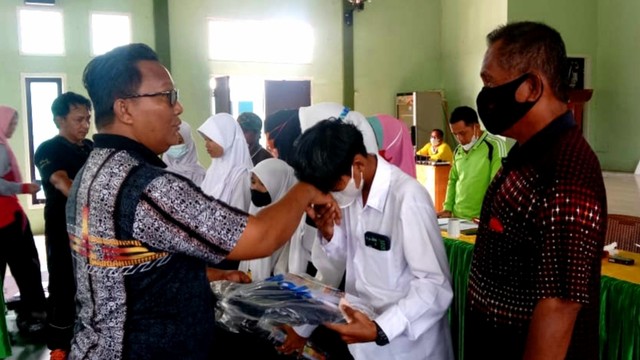 Kepala Desa Batu Belaman, Rudi Hartono menyerahkan bantuan perlengkapan sekolah gratis untuk pelajar yang berasal dari keluarga kurang mampu di desanya. Foto: IST/InfoPBUN