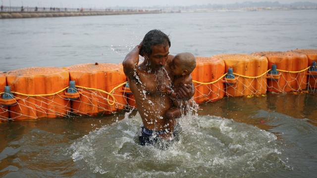 Seorang umat Hindu berenang saat menggendong putranya di Sangam, pertemuan sungai Gangga, Yamuna dan Saraswati selama festival Magh Mela, di Prayagraj, India, Jumat (14/1). Foto: Ritesh Shukla/REUTERS