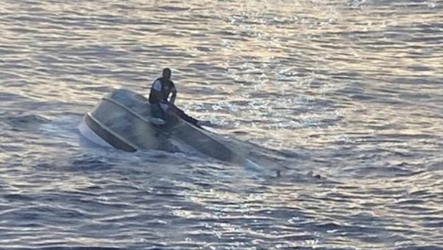 Seorang pria duduk di atas kapal yang terbalik di lepas pantai Fort Pierce Inlet, Florida, Amerika Serikat, Selasa (25/1/2022). Foto: US Coast Guard/via REUTERS