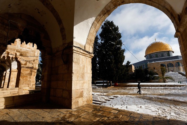 Seorang pria berjalan melewati Kubah Batu, yang terletak di Kota Tua Yerusalem di kompleks yang oleh umat Islam dikenal sebagai Suaka Mulia dan bagi orang Yahudi sebagai Bukit Bait Suci selama pagi bersalju di Kota Tua Yerusalem, 27 Januari 2022. Foto: REUTERS/Ammar Awad
