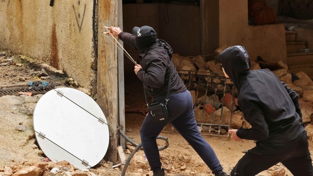 Pria Palestina terlibat bentrok dan menembakkan katapel ke arah pasukan keamanan Israel yang membongkar rumah Abu Shkhaydam di Yerusalem, Selasa (1/2/2022). Foto: Hazem Bader/AFP