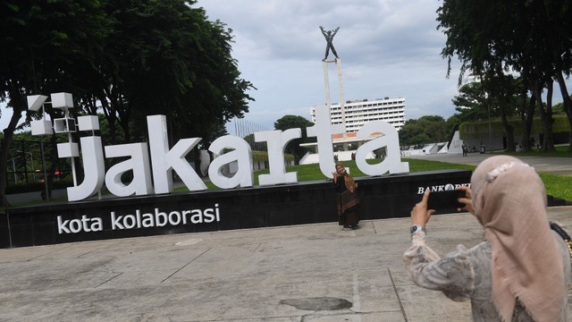 Seorang warga menurunkan maskernya saat berfoto di Taman Lapangan Banteng, Jakarta, Minggu (6/2/2022). Foto: Akbar Nugroho Gumay/Antara Foto